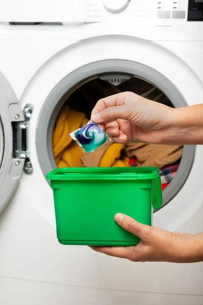 Woman putting laundry detergent capsule into washing machine indoors, closeup.Colorful laundry eco gel in capsule. Washing clothes.The concept of washing and cleanliness