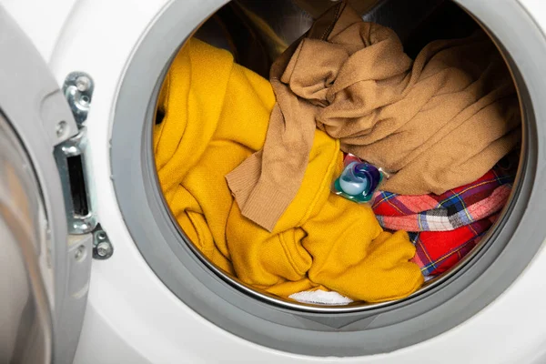 laundry detergent capsule into washing machine indoors, closeup.Colorful laundry eco gel in capsule. Washing clothers.The concept of washing and cleanliness