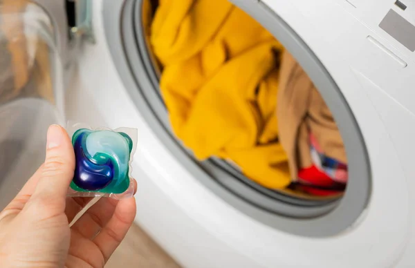 Woman putting laundry detergent capsule into washing machine indoors, closeup.Colorful laundry eco gel in capsule. Washing clothes.The concept of washing and cleanliness