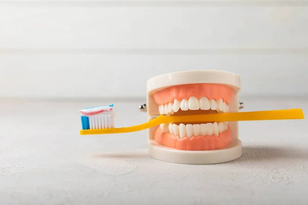 Dentures with a yellow toothbrush on a white wooden background. Upper and lower jaws with false teeth. Dentures or false teeth, close-up. copy space.Prevention of caries.MOCKUP