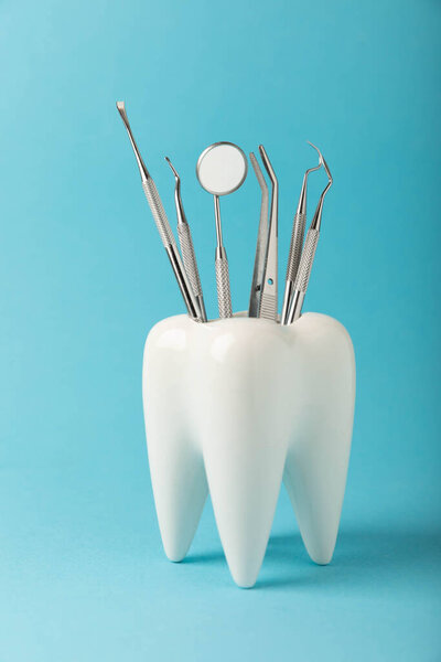 White healthy tooth and various dental tools for dental care.Dental concept.Composition on a blue background.Side view. Copy space.MOCKUP.Dental hygiene.