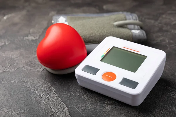 Digital blood pressure monitor and heart on black marble background.Medical equipment blood pressure monitor.Health care. Place for text. Medicine concept. The concept of cardiology.