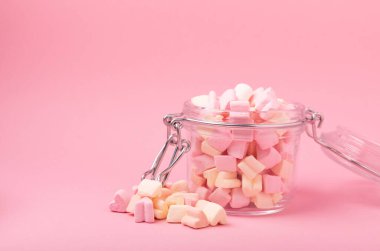 Pembe arka planda cam bir kavanozda lokum. Meyve aromalı tatlılar. Çilekli lokum. Uzayı kopyala. Metin için yer