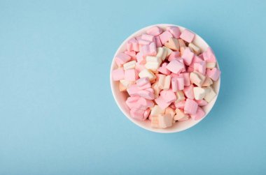 Mavi bir arka planda tabakta marşmelovlar. Çilek aromalı yakın plan şeker, partiler için abur cubur, kahve ve kakao. Kış yiyecekleri konsepti için yer..