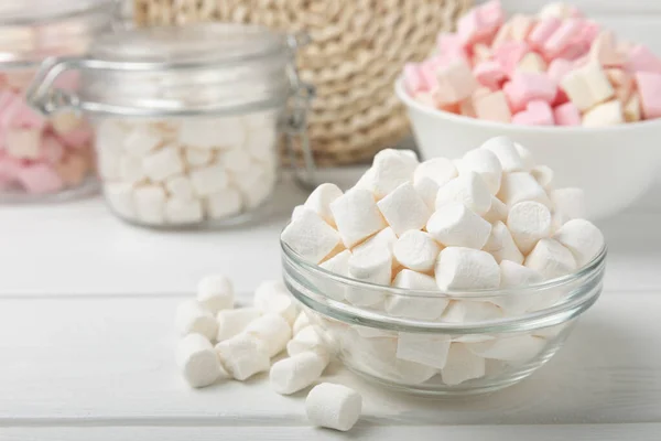 Many different marshmallows in bowls and jars on a white textured wood. White and fruit marshmallow. Sweets and snacks for a snack. Chewing candies close-up. Copy space. Place for text.