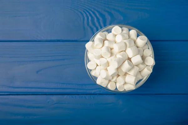Marshmallow on blue textured wood. White marshmallows in a glass bowl and a jar on the table.Sweets and snacks for a snack. Chewing candies close-up. Copy space. Place for text. Winter food concept.