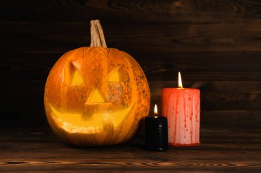 Kahverengi ahşap desenli Cadılar Bayramı balkabağı ve mumlar. Karanlık bir arka planda kompozisyon. Parlayan gözleri ve ağzı olan korkutucu bir kompozisyon. Tatil konsepti. Boşluğu kopyala