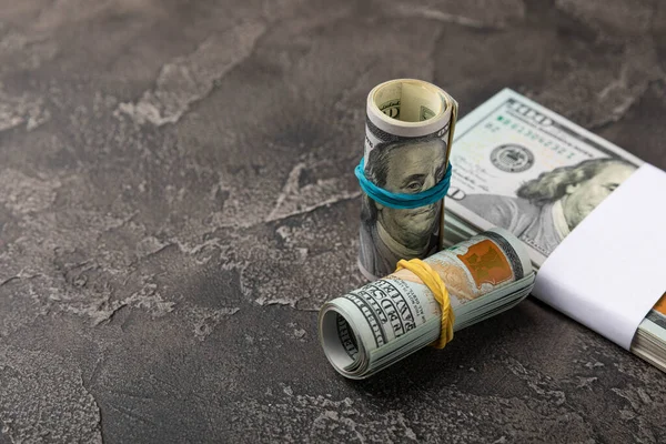 Money, a roll of US hundred dollar bills on a black texture background. Money is scattered on the table. Concepts of finance and economy. Money accumulation concept. Saving currency. Investments.