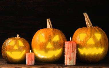 Kahverengi ahşap desenli Cadılar Bayramı balkabağı ve mumlar. Karanlık bir arka planda kompozisyon. Parlayan gözleri ve ağzı olan korkutucu bir kompozisyon. Tatil konsepti. Boşluğu kopyala