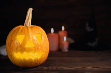 Kahverengi ahşap desenli Cadılar Bayramı balkabağı ve mumlar. Karanlık bir arka planda kompozisyon. Parlayan gözleri ve ağzı olan korkutucu bir kompozisyon. Tatil konsepti. Boşluğu kopyala