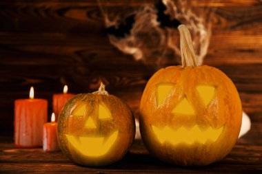 Kahverengi ahşap desenli Cadılar Bayramı balkabağı ve mumlar. Karanlık bir arka planda kompozisyon. Parlayan gözleri ve ağzı olan korkutucu bir kompozisyon. Tatil konsepti. Boşluğu kopyala