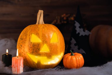 Kahverengi ahşap desenli Cadılar Bayramı balkabağı ve mumlar. Karanlık bir arka planda kompozisyon. Parlayan gözleri ve ağzı olan korkutucu bir kompozisyon. Tatil konsepti. Boşluğu kopyala