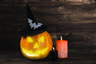 Kahverengi ahşap desenli Cadılar Bayramı balkabağı ve mumlar. Karanlık bir arka planda kompozisyon. Parlayan gözleri ve ağzı olan korkutucu bir kompozisyon. Tatil konsepti. Boşluğu kopyala