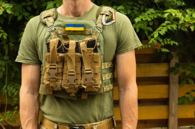 Kamuflaj taktik üniformalı bir asker ve arka planda ahşap ve yeşillik kaplı bir askeri zırh. Çatışma izmaritli vücut zırhı. Ukrayna ordusu. Askeri bir kavram. Savaş yok. Tıbbi turnike..