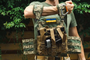 Kamuflaj taktik üniformalı bir asker ve arka planda ahşap ve yeşillik kaplı bir askeri zırh. Çatışma izmaritli vücut zırhı. Ukrayna ordusu. Askeri bir kavram. Savaş yok. Tıbbi turnike..