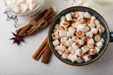 Bir fincan lezzetli kakao içeceği ve mavi bardakta şekerlemeler. Beyaz dokuma masasında kış içecekleri için şekerlemeler ve şekerlemeler. Kış sıcak içeceği. Şekerleme ve baharatlı sıcak çikolata..