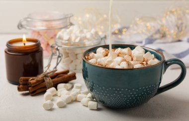 Bir fincan lezzetli kakao içeceği ve mavi bardakta şekerlemeler. Beyaz dokuma masasında kış içecekleri için şekerlemeler ve şekerlemeler. Kış sıcak içeceği. Şekerleme ve baharatlı sıcak çikolata..