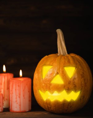 Kahverengi ahşap desenli Cadılar Bayramı balkabağı ve mumlar. Karanlık bir arka planda kompozisyon. Parlayan gözleri ve ağzı olan korkutucu bir kompozisyon. Tatil konsepti. Boşluğu kopyala