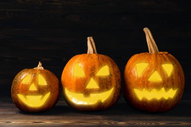 Kahverengi ahşap desenli Cadılar Bayramı balkabağı. Karanlık bir arka planda kompozisyon. Parlayan gözleri ve ağzı olan korkutucu bir kompozisyon. Tatil konsepti. Boşluğu kopyala