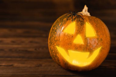 Kahverengi ahşap desenli Cadılar Bayramı balkabağı. Karanlık bir arka planda kompozisyon. Parlayan gözleri ve ağzı olan korkutucu bir kompozisyon. Tatil konsepti. Boşluğu kopyala