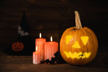 Kahverengi ahşap desenli Cadılar Bayramı balkabağı ve mumlar. Karanlık bir arka planda kompozisyon. Parlayan gözleri ve ağzı olan korkutucu bir kompozisyon. Tatil konsepti. Boşluğu kopyala