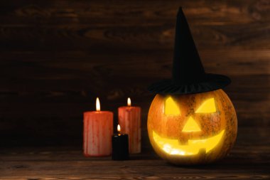 Kahverengi ahşap desenli Cadılar Bayramı balkabağı ve mumlar. Karanlık bir arka planda kompozisyon. Parlayan gözleri ve ağzı olan korkutucu bir kompozisyon. Tatil konsepti. Boşluğu kopyala