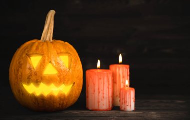 Kahverengi ahşap desenli Cadılar Bayramı balkabağı ve mumlar. Karanlık bir arka planda kompozisyon. Parlayan gözleri ve ağzı olan korkutucu bir kompozisyon. Tatil konsepti. Boşluğu kopyala