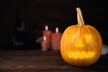 Kahverengi ahşap desenli Cadılar Bayramı balkabağı ve mumlar. Karanlık bir arka planda kompozisyon. Parlayan gözleri ve ağzı olan korkutucu bir kompozisyon. Tatil konsepti. Boşluğu kopyala