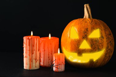 Kahverengi ahşap desenli Cadılar Bayramı balkabağı ve mumlar. Karanlık bir arka planda kompozisyon. Parlayan gözleri ve ağzı olan korkutucu bir kompozisyon. Tatil konsepti. Boşluğu kopyala