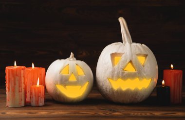 Kahverengi ahşap desenli Cadılar Bayramı balkabağı ve mumlar. Karanlık bir arka planda kompozisyon. Parlayan gözleri ve ağzı olan korkutucu bir kompozisyon. Tatil konsepti. Boşluğu kopyala