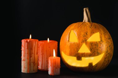 Kahverengi ahşap desenli Cadılar Bayramı balkabağı ve mumlar. Karanlık bir arka planda kompozisyon. Parlayan gözleri ve ağzı olan korkutucu bir kompozisyon. Tatil konsepti. Boşluğu kopyala