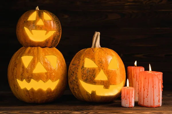 Kahverengi ahşap desenli Cadılar Bayramı balkabağı ve mumlar. Karanlık bir arka planda kompozisyon. Parlayan gözleri ve ağzı olan korkutucu bir kompozisyon. Tatil konsepti. Boşluğu kopyala