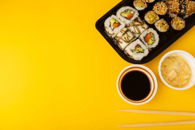 Sarı arka planda tek kullanımlık kutularda lezzetli suşi ruloları. Yemek teslimatı konsepti. Ofiste yemek var. Japon yemeği. Düz görünüm, metin için boşluk ve kopyalama alanı ile yatıyordu.