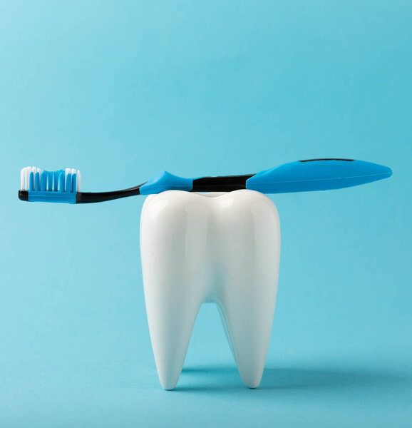 Cleaning model of a white tooth with a toothbrush on a blue background. The concept of dental hygiene. Prevention of plaque and gum disease.MOCKUP