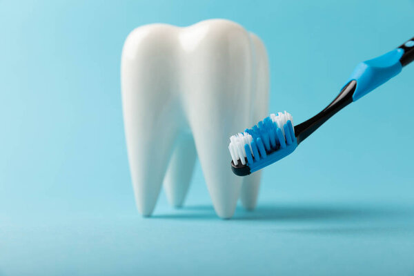 Cleaning model of a white tooth with a toothbrush on a blue background. The concept of dental hygiene. Prevention of plaque and gum disease.Prevention of caries.MOCKUP