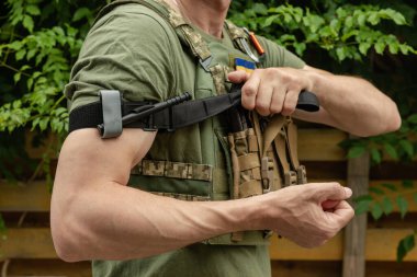 Bir asker, ilk yardımda kanı durdurmak ve kanamayı önlemek için elinde tıbbi bir turnike tutuyor. Savaş taktik ekipmanları. Savaş kullanımı Turnstil.