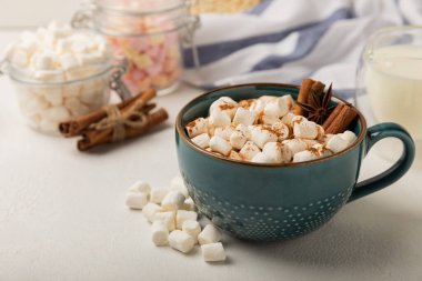 Bir fincan lezzetli kakao içeceği ve mavi bardakta şekerlemeler. Beyaz dokuma masasında kış içecekleri için şekerlemeler ve şekerlemeler. Kış sıcak içeceği. Şekerleme ve baharatlı sıcak çikolata..