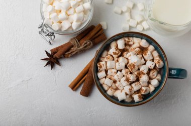 Bir fincan lezzetli kakao içeceği ve mavi bardakta şekerlemeler. Beyaz dokuma masasında kış içecekleri için şekerlemeler ve şekerlemeler. Kış sıcak içeceği. Şekerleme ve baharatlı sıcak çikolata..