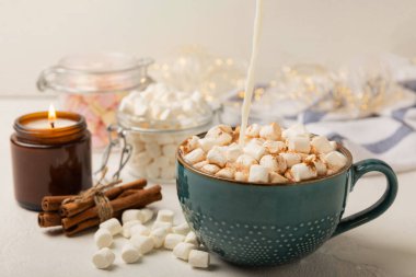 Bir fincan lezzetli kakao içeceği ve mavi bardakta şekerlemeler. Beyaz dokuma masasında kış içecekleri için şekerlemeler ve şekerlemeler. Kış sıcak içeceği. Şekerleme ve baharatlı sıcak çikolata..