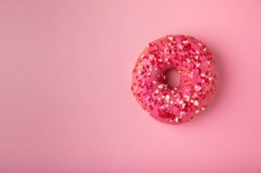 Pembe bir arka planda donut. Üzerinde pembe krema ve kağıt kaplama serpiştirilmiş meyveli çörek. Renkli minimalizm kavramı. Çöp yiyecekler..