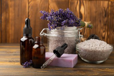 Lavanta kaplıcası. Temel yağlar, deniz tuzu, vücut fırçası, lavanta çiçekleri ve el yapımı sabun. Kahverengi dokuda lavanta çiçekleri bulunan doğal bitkisel kozmetik ürünleri..