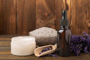 Lavanta kaplıcası. Temel yağlar, deniz tuzu, vücut fırçası, lavanta çiçekleri ve el yapımı sabun. Kahverengi dokuda lavanta çiçekleri bulunan doğal bitkisel kozmetik ürünleri..