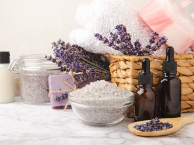Lavanta kaplıcası. Temel yağlar, deniz tuzu, vücut fırçası, lavanta çiçekleri ve el yapımı sabun. Mermer arka planda lavanta çiçekleri bulunan doğal bitkisel kozmetik ürünleri..