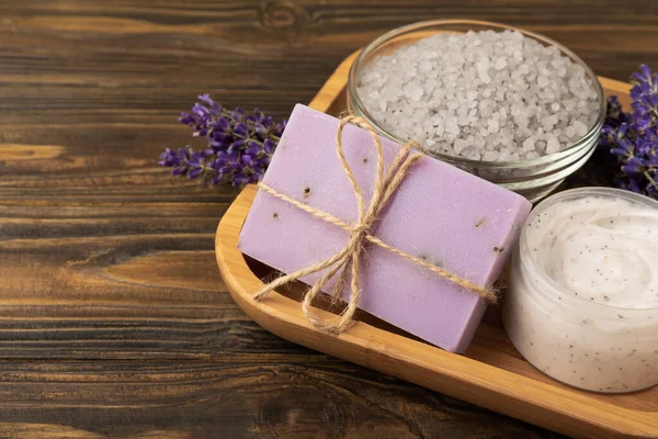 Lavender spa. Sea salt, body scrub, lavender flowers and handmade soap. Natural herbal cosmetics with lavender flowers on brown texture wood.Spa and relaxation concept.Beauty treatments.Copy space.