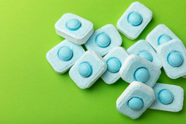 Yeşil arka planda su yumuşatıcı tabletler, düz. Ders için yer. Çamaşır makineleri için kapsüller ve kireç ölçeği önleyen bulaşık makineleri için. Kopyalanacak yer.