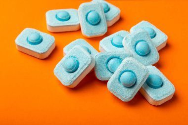 Turuncu arka planda su yumuşatıcı tabletler, düz. Ders için yer. Çamaşır makineleri için kapsüller ve kireç ölçeği önleyen bulaşık makineleri için. Kopyalanacak yer.