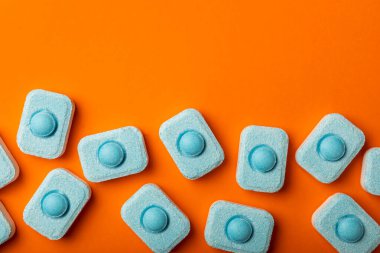 Turuncu arka planda su yumuşatıcı tabletler, düz. Ders için yer. Çamaşır makineleri için kapsüller ve kireç ölçeği önleyen bulaşık makineleri için. Kopyalanacak yer.