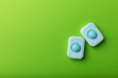 Yeşil arka planda su yumuşatıcı tabletler, düz. Ders için yer. Çamaşır makineleri için kapsüller ve kireç ölçeği önleyen bulaşık makineleri için. Kopyalanacak yer.