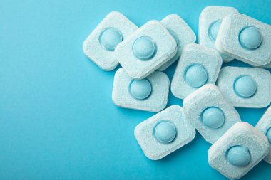 Mavi arka planda su yumuşatıcı tabletler, düz. Ders için yer. Çamaşır makineleri için kapsüller ve kireç ölçeği önleyen bulaşık makineleri için. Kopyalanacak yer.