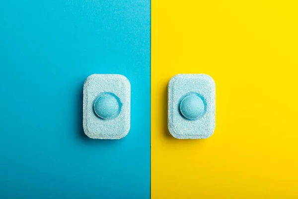 Water softener tablets on yellow-blue background, flat lay. Space for text.Capsules for washing machines and dishwashers that prevent limescale. Place to copy.